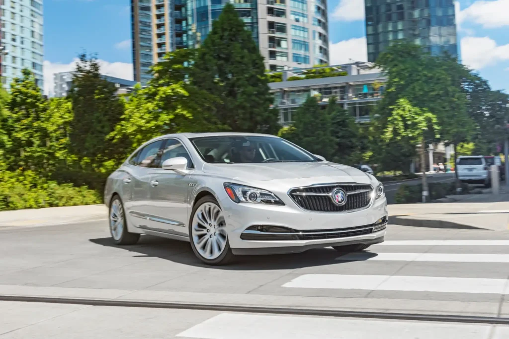 2017 Buick LaCrosse silver sedan front three quarter view driving on urban road with modern buildings in background 2017 Buick LaCrosse silver sedan front three quarter view driving on urban road with modern buildings in background
