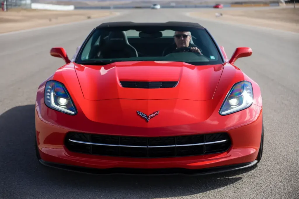 2014 Corvette Stingray Z51 Convertible head on with headlights illuminated driver visible black soft top performance bumper aerodynamic hood vent 2014 Corvette Stingray Z51 Convertible head on with headlights illuminated driver visible black soft top performance bumper aerodynamic hood vent