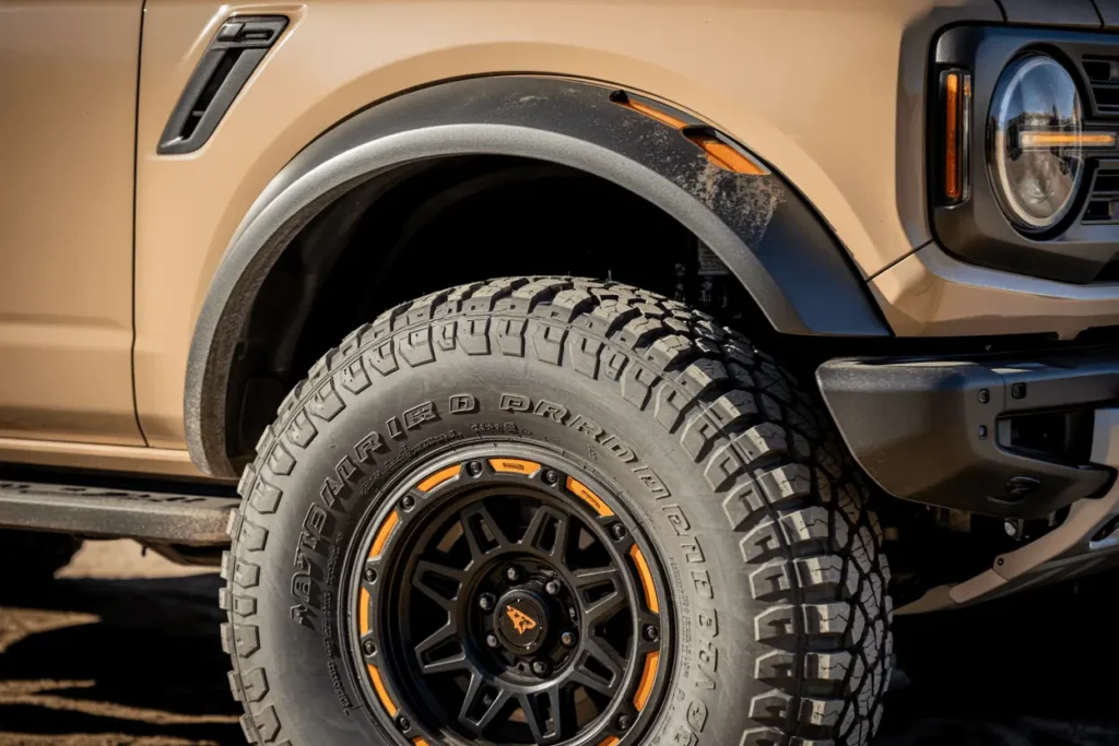 Close up wheel detail of the 2025 Ford Bronco Raptor showing beadlock style rim all terrain tire tread and rugged fender arch Close up wheel detail of the 2025 Ford Bronco Raptor showing beadlock style rim all terrain tire tread and rugged fender arch