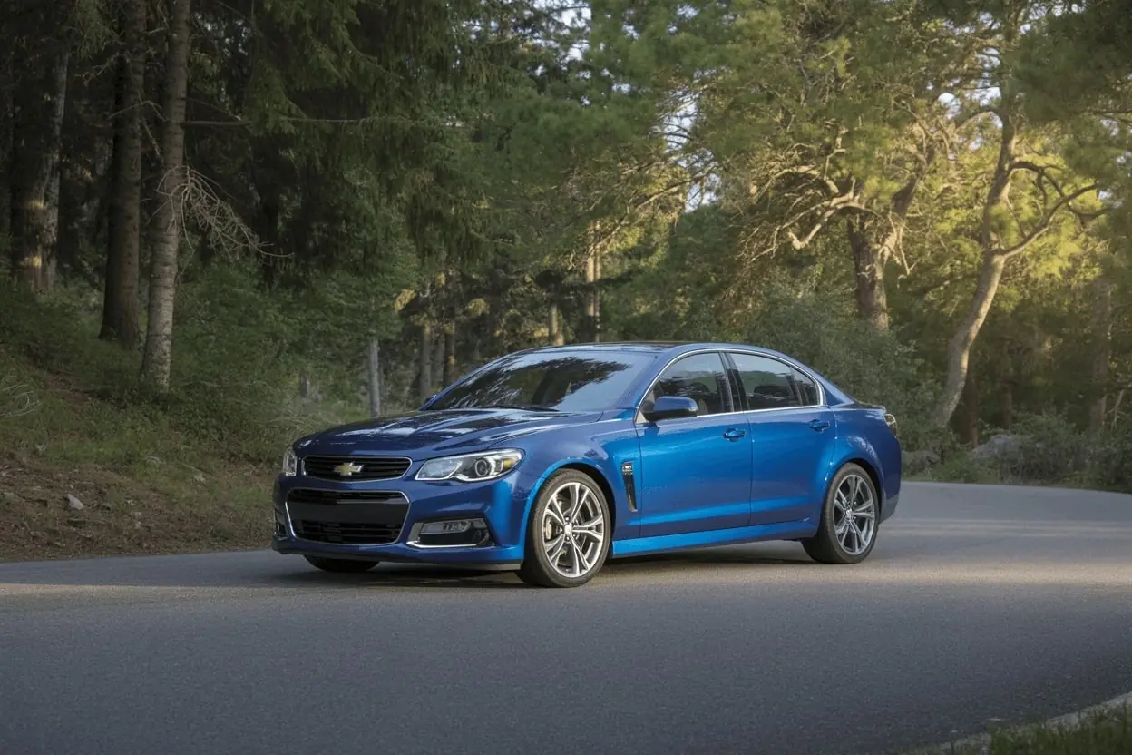 Front three-quarter shot of blue 2016 Chevrolet SS sports sedan parked on quiet forest curve under soft evening light.