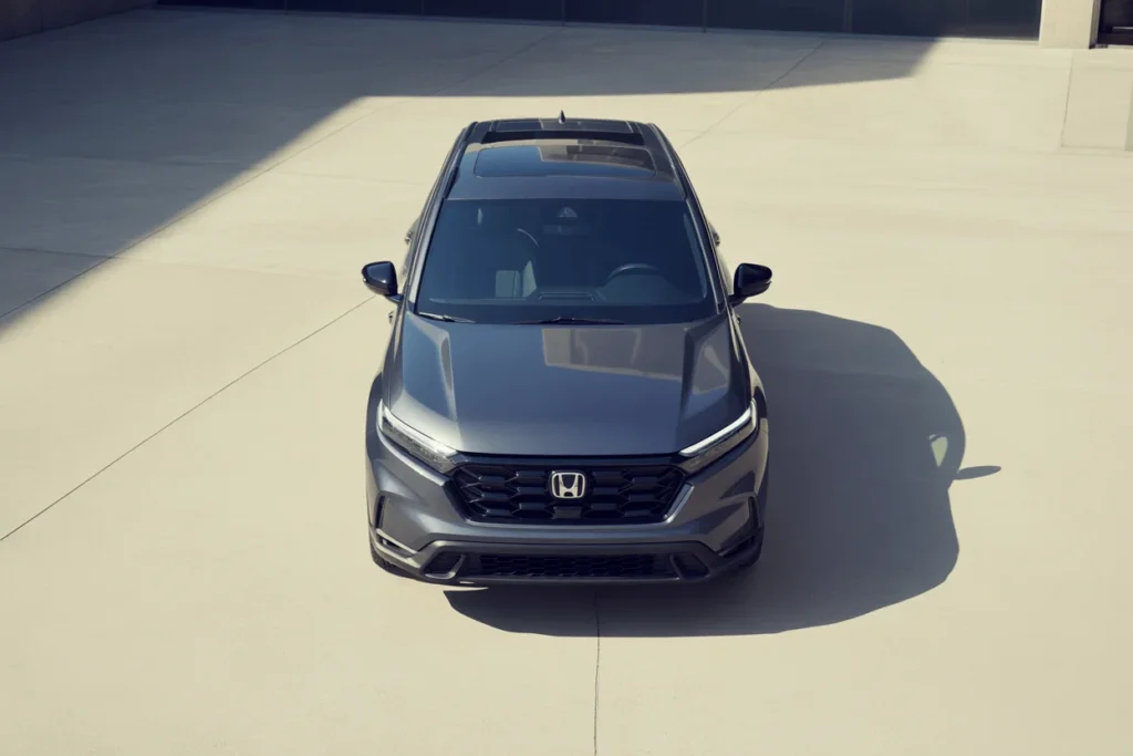 High front view of 2025 Honda CR V SUV in gray sunlit plaza highlighting panoramic roof and sculpted hood High front view of 2025 Honda CR V SUV in gray sunlit plaza highlighting panoramic roof and sculpted hood