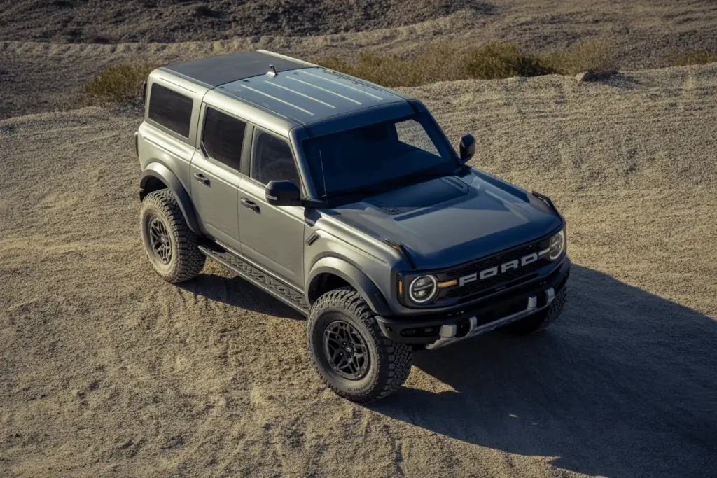 Overhead angle of grey 2025 Ford Bronco Raptor on rugged ground highlighting roof design off road stance and black fender flares Overhead angle of grey 2025 Ford Bronco Raptor on rugged ground highlighting roof design off road stance and black fender flares