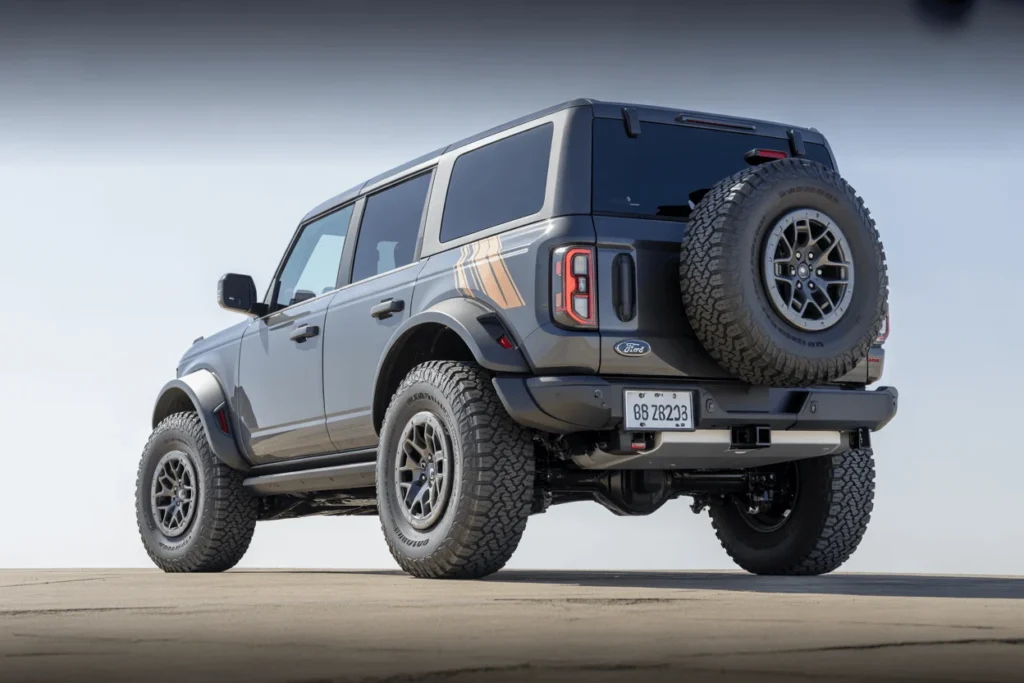 Rear three quarter angle of the 2025 Ford Bronco Raptor in grey showcasing spare tire taillights and wide off road stance Rear three quarter angle of the 2025 Ford Bronco Raptor in grey showcasing spare tire taillights and wide off road stance