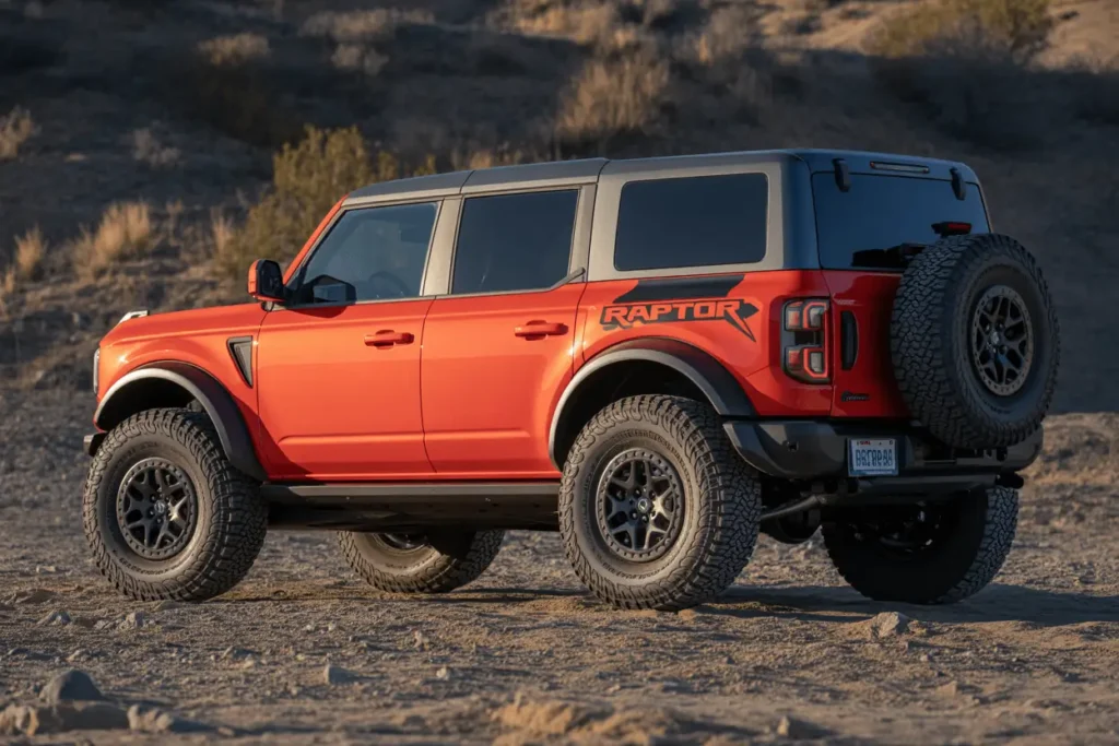 Rear three quarter view of an orange 2025 Ford Bronco Raptor on desert ground featuring bold Raptor graphics and black alloy wheels Rear three quarter view of an orange 2025 Ford Bronco Raptor on desert ground featuring bold Raptor graphics and black alloy wheels