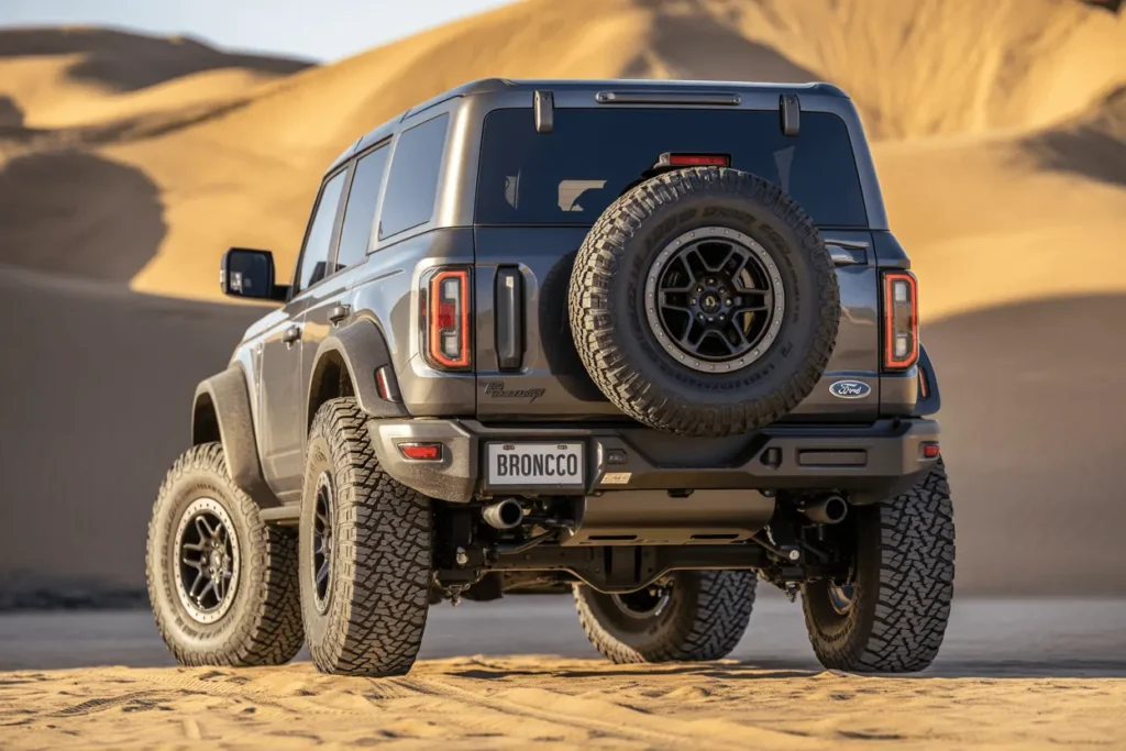 Rear view of grey 2025 Ford Bronco Raptor in sand dunes displaying spare wheel LED taillights and elevated suspension Rear view of grey 2025 Ford Bronco Raptor in sand dunes displaying spare wheel LED taillights and elevated suspension