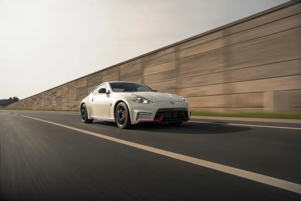 2014 Nissan 370Z Nismo front three quarter view at speed on open freeway pearl white body black wheels red lip 2014 Nissan 370Z Nismo front three quarter view at speed on open freeway pearl white body black wheels red lip