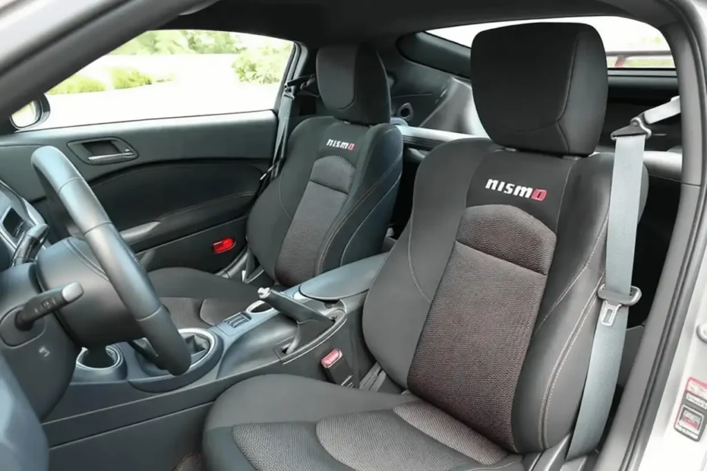 2014 Nissan 370Z Nismo interior side view bolstered Nismo front bucket seats dark upholstery visible seatbelt and center console 2014 Nissan 370Z Nismo interior side view bolstered Nismo front bucket seats dark upholstery visible seatbelt and center console
