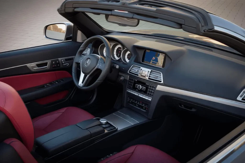 Angled cockpit view of 2014 Mercedes Benz E350 Cabriolet red leather seats navigation screen open top on sunlit paved lot Angled cockpit view of 2014 Mercedes Benz E350 Cabriolet red leather seats navigation screen open top on sunlit paved lot