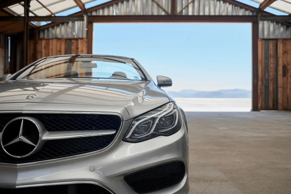 Front right detail view of 2014 Mercedes Benz E350 Cabriolet in open barn highlighting projector headlights and chrome grille against mountains Front right detail view of 2014 Mercedes Benz E350 Cabriolet in open barn highlighting projector headlights and chrome grille against mountains