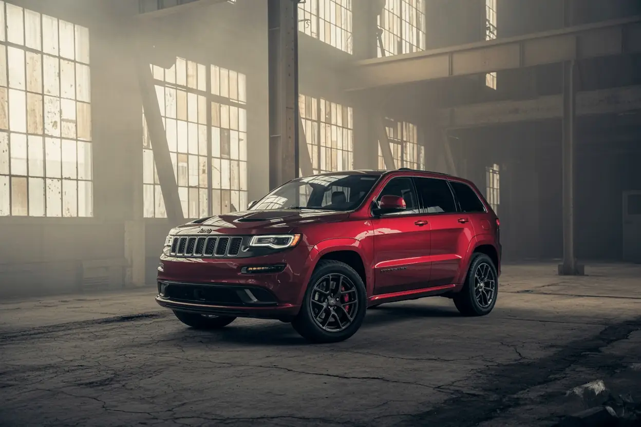 Front three-quarter view of 2016 Jeep Grand Cherokee SRT in red, under moody warehouse light with cracked floor.