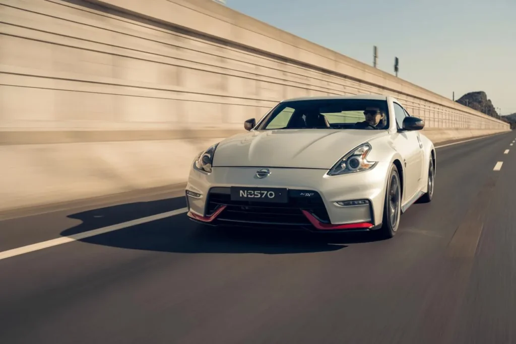 Head on front view of 2014 Nissan 370Z Nismo on sunlit expressway pearl white coupe red Nismo lip sporty stance Head on front view of 2014 Nissan 370Z Nismo on sunlit expressway pearl white coupe red Nismo lip sporty stance