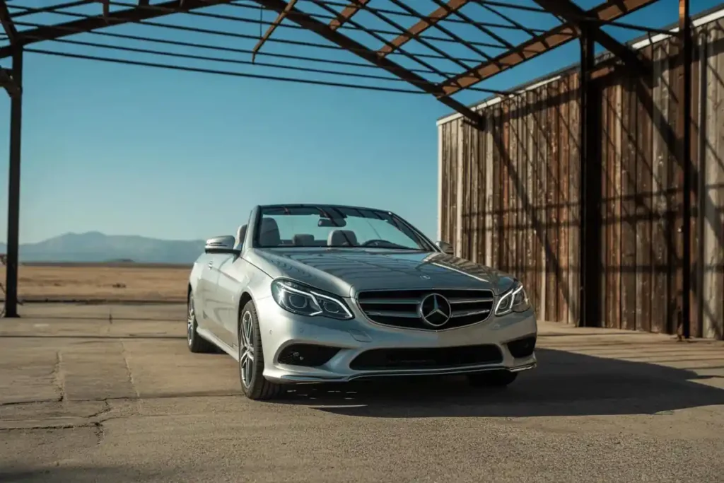 Low front three quarter angle of 2014 Mercedes Benz E350 Cabriolet under open steel roof emphasizing LED headlights and sculpted hood Low front three quarter angle of 2014 Mercedes Benz E350 Cabriolet under open steel roof emphasizing LED headlights and sculpted hood