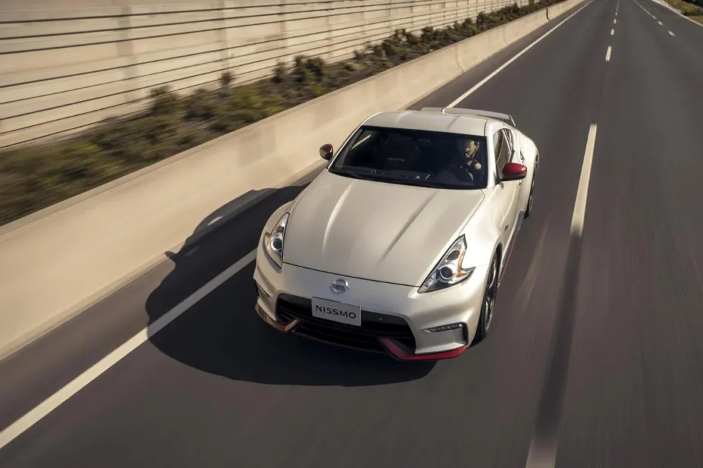 Overhead front three quarter view of 2014 Nissan 370Z Nismo on empty highway pearl white paint red mirror caps Overhead front three quarter view of 2014 Nissan 370Z Nismo on empty highway pearl white paint red mirror caps