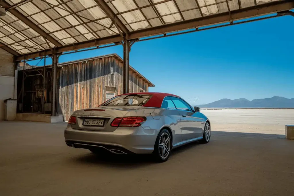 Rear three quarter view of 2014 Mercedes Benz E350 Cabriolet with red soft top beside rustic warehouse overlooking dry lake Rear three quarter view of 2014 Mercedes Benz E350 Cabriolet with red soft top beside rustic warehouse overlooking dry lake