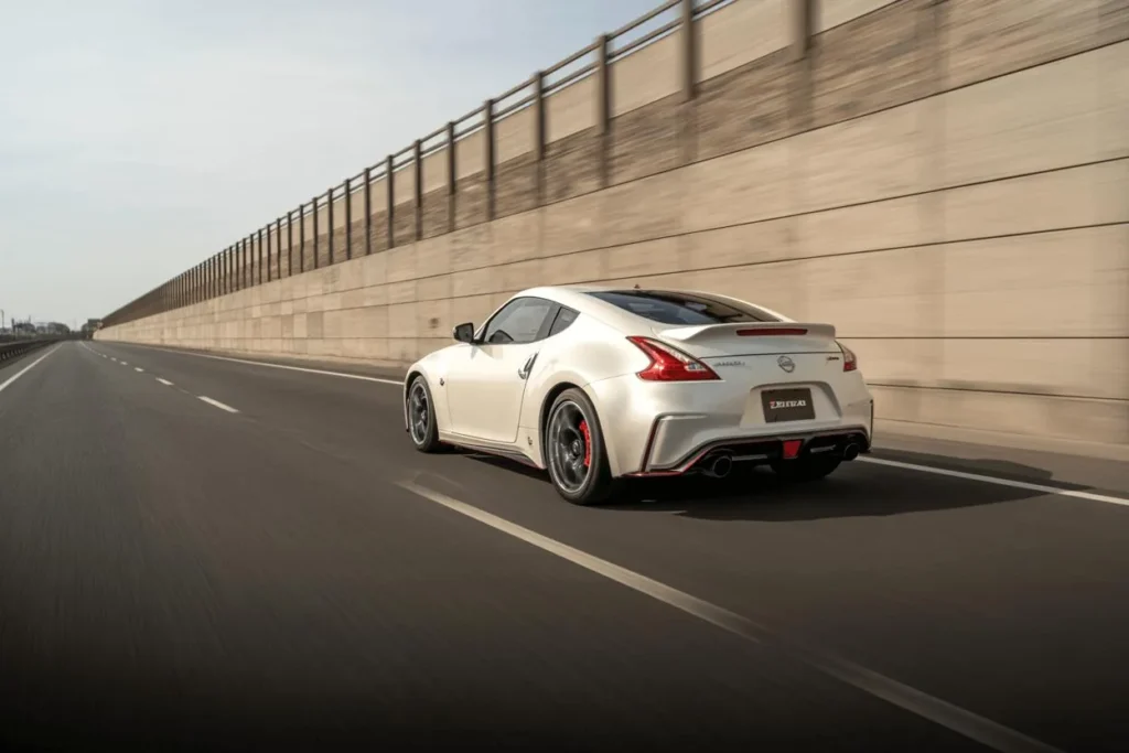 Rear three quarter view of 2014 Nissan 370Z Nismo on deserted highway pearl white coupe rear spoiler dual exhaust red diffuser Rear three quarter view of 2014 Nissan 370Z Nismo on deserted highway pearl white coupe rear spoiler dual exhaust red diffuser