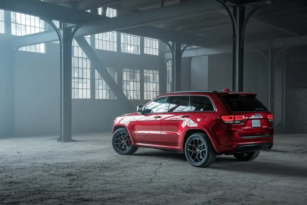 Rear three quarter view of 2016 Jeep Grand Cherokee SRT in red parked in foggy industrial warehouse setting Rear three quarter view of 2016 Jeep Grand Cherokee SRT in red parked in foggy industrial warehouse setting