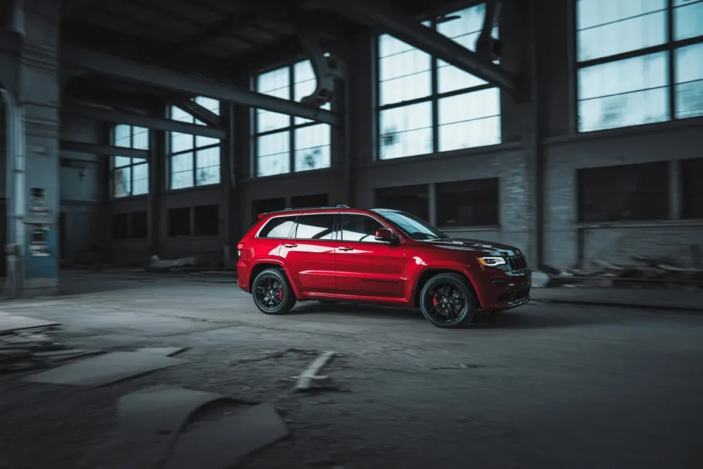 Side profile action shot of 2016 Jeep Grand Cherokee SRT red performance SUV driving through abandoned industrial warehouse Side profile action shot of 2016 Jeep Grand Cherokee SRT red performance SUV driving through abandoned industrial warehouse