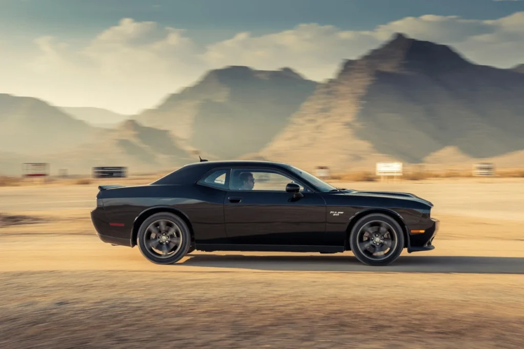 Side profile of 2013 Dodge Challenger RT Plus rolling along desert road showcasing long coupe roofline and dark wheels Side profile of 2013 Dodge Challenger RT Plus rolling along desert road showcasing long coupe roofline and dark wheels