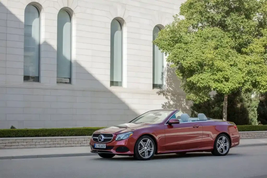 Wide side profile front left shot of 2015 Mercedes Benz E400 Cabriolet top down silver alloys sunlit stone arches tree Wide side profile front left shot of 2015 Mercedes Benz E400 Cabriolet top down silver alloys sunlit stone arches tree