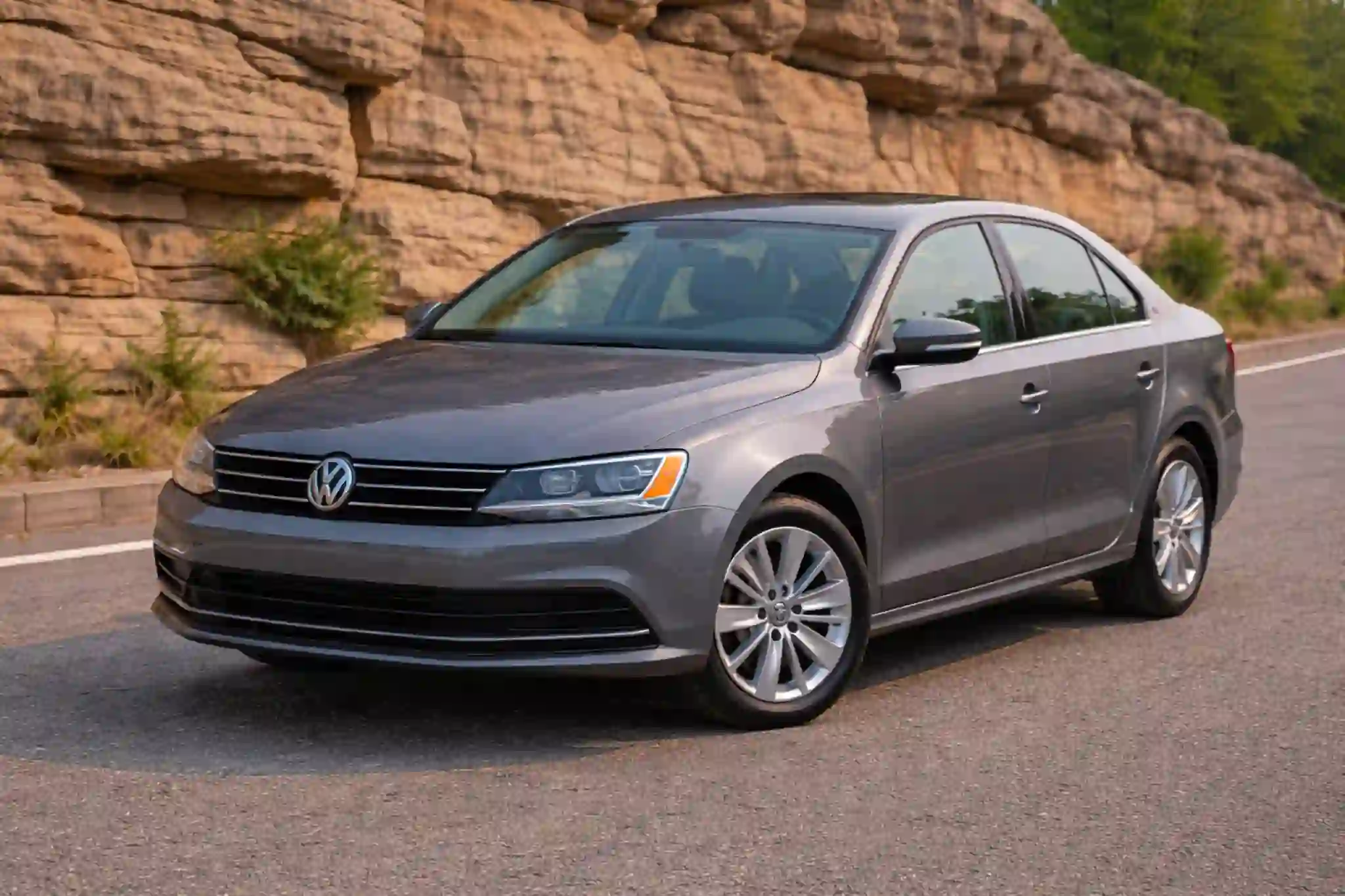 A gray 2015 Volkswagen Jetta 1.8T SE is viewed from a high front angle emphasizing the hood windshield and VW grille centered on the roadway
